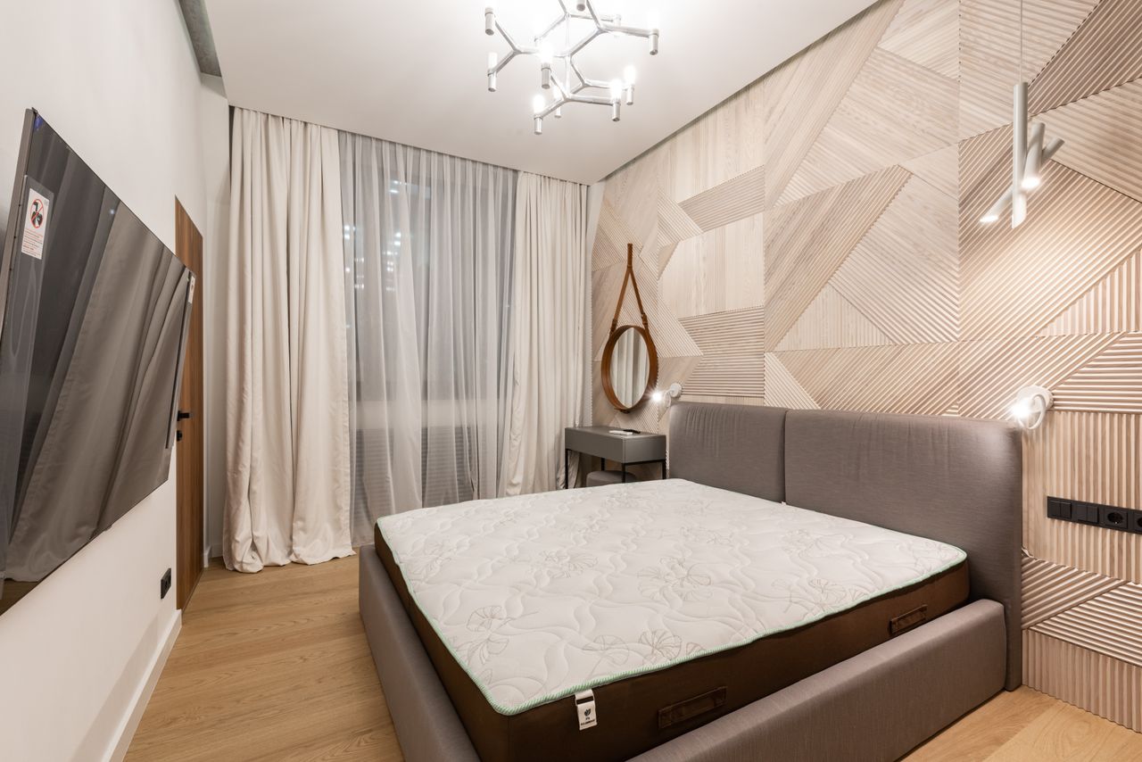 about-us-02 Comfortable bed with mattress placed in front of modern TV in cozy bedroom with creative lamps and wooden floor