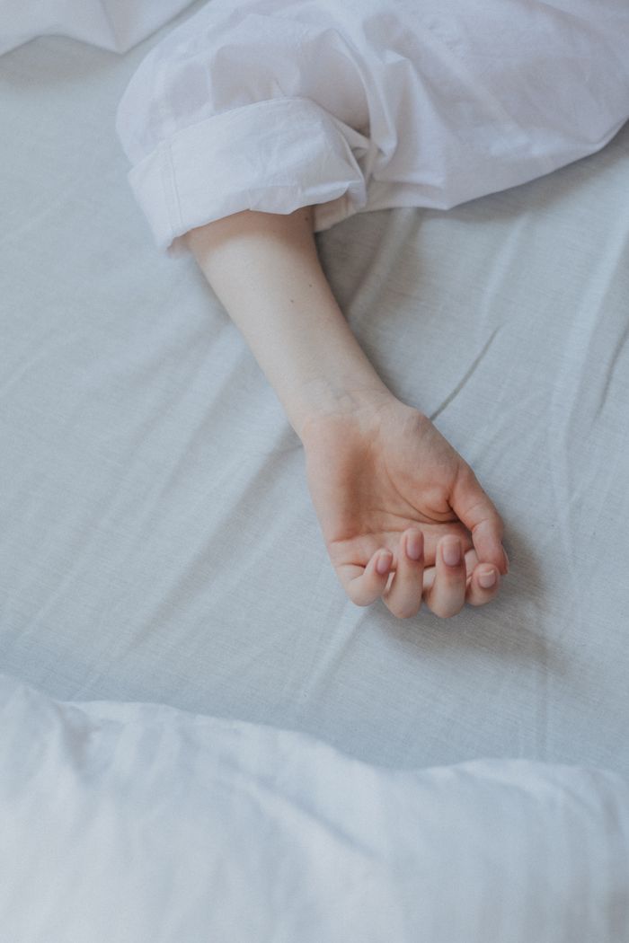 Close-up of a relaxed arm resting on a white bed sheet, suggesting tranquility.
